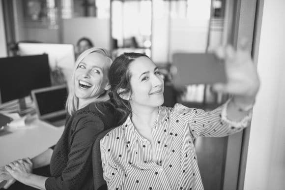Coworkers taking selfies at work as part of a broader employer branding strategy.