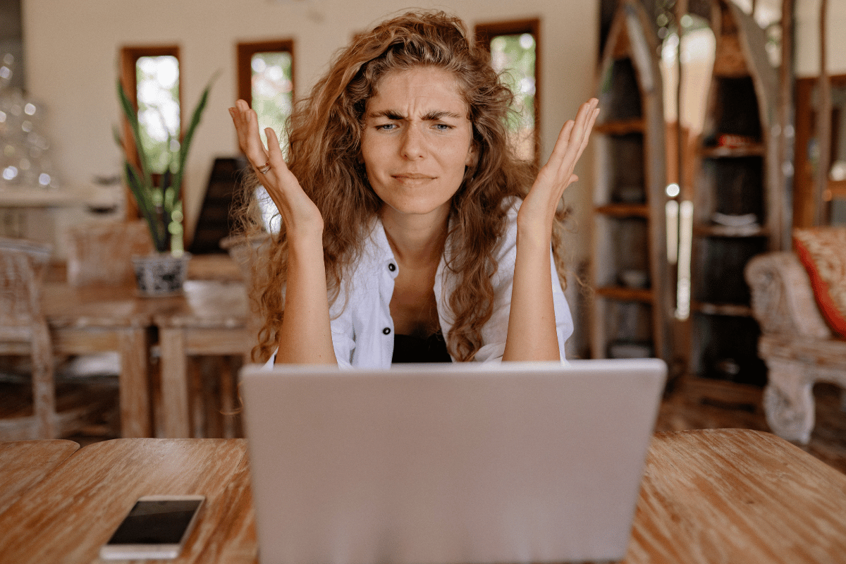 frustrated woman throws her hands up while sitting in front of her laptop